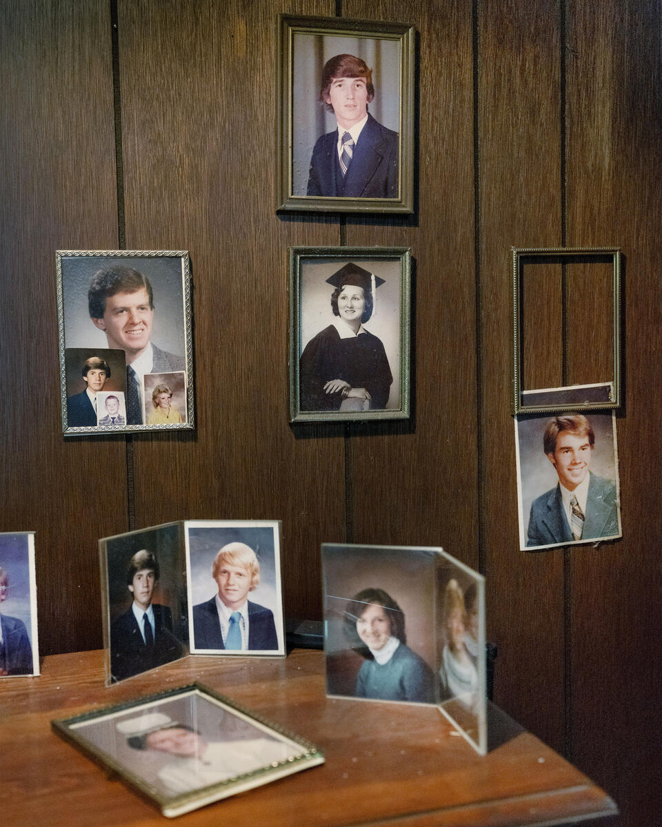 Framed photographs mounted on a wood-paneled wall of men and women in various portraits. A sidetable below features additional photographs.