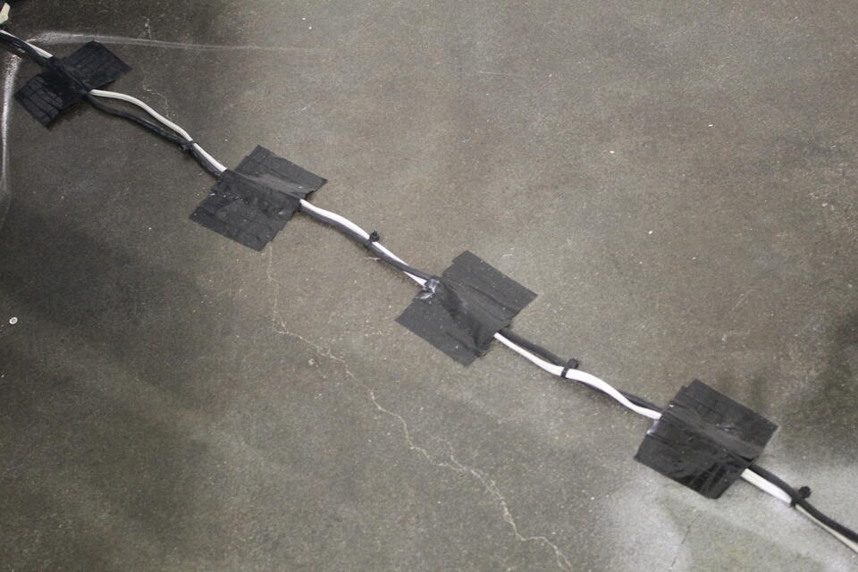 One black wire and one white wire are taped deliberately along the floor with black electrical tape.