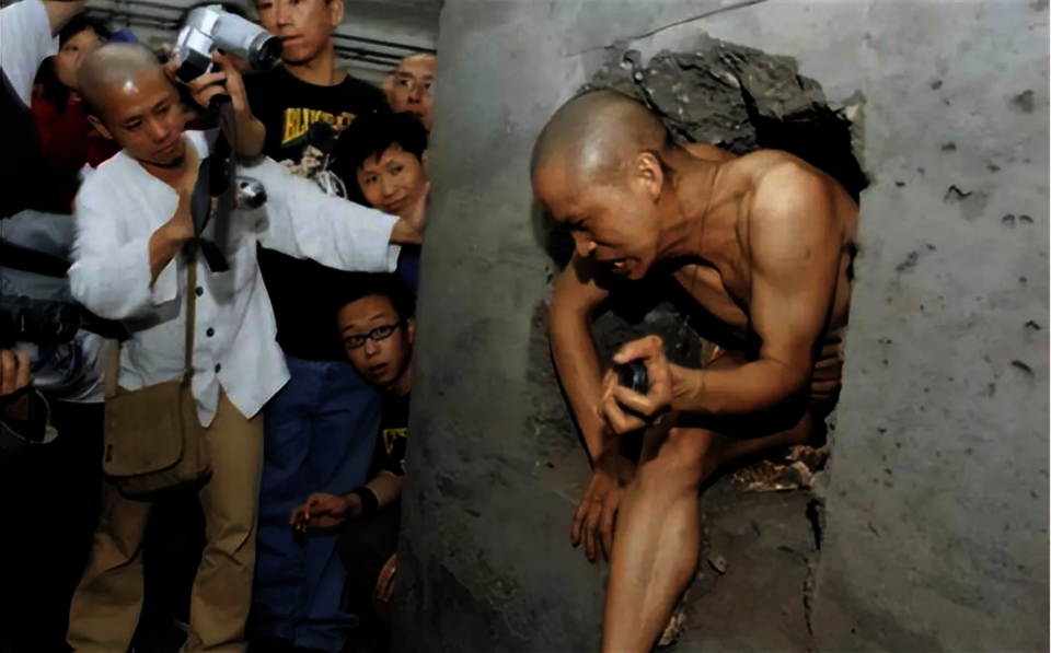 The artist is trying to get out of a hollow cement pillar after he sealed himself inside for twenty four hours.