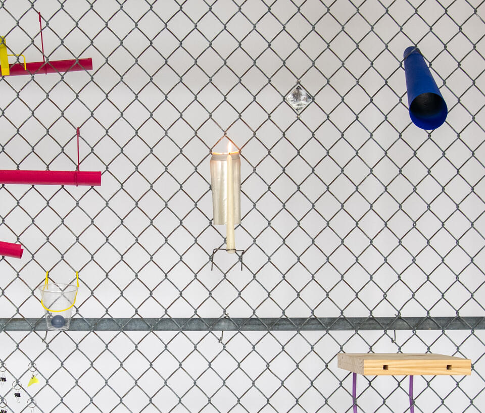 Close up of a chain link fence with various designed objects affixed to it, including a candle holder and a blue telescope.