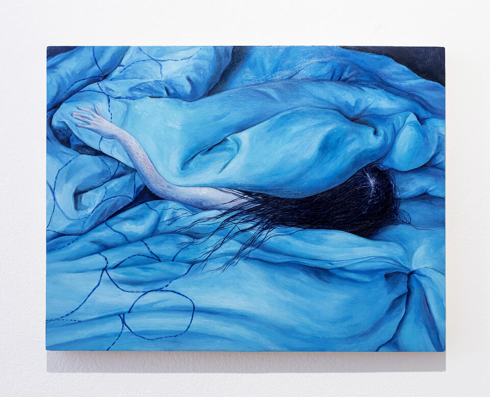 A human arm and head with long black hair pokes out of a blue duvet blanket that takes up the entire composition
