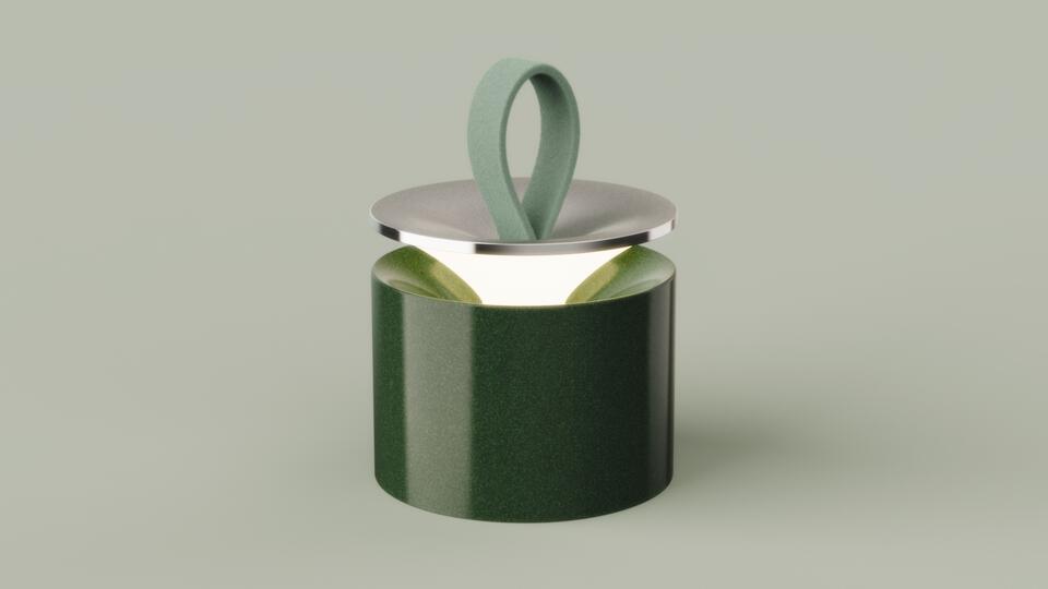 A glossy green ceramic lamp with a soft felt loop handle and lifted metal lid, glowing warmly from within.