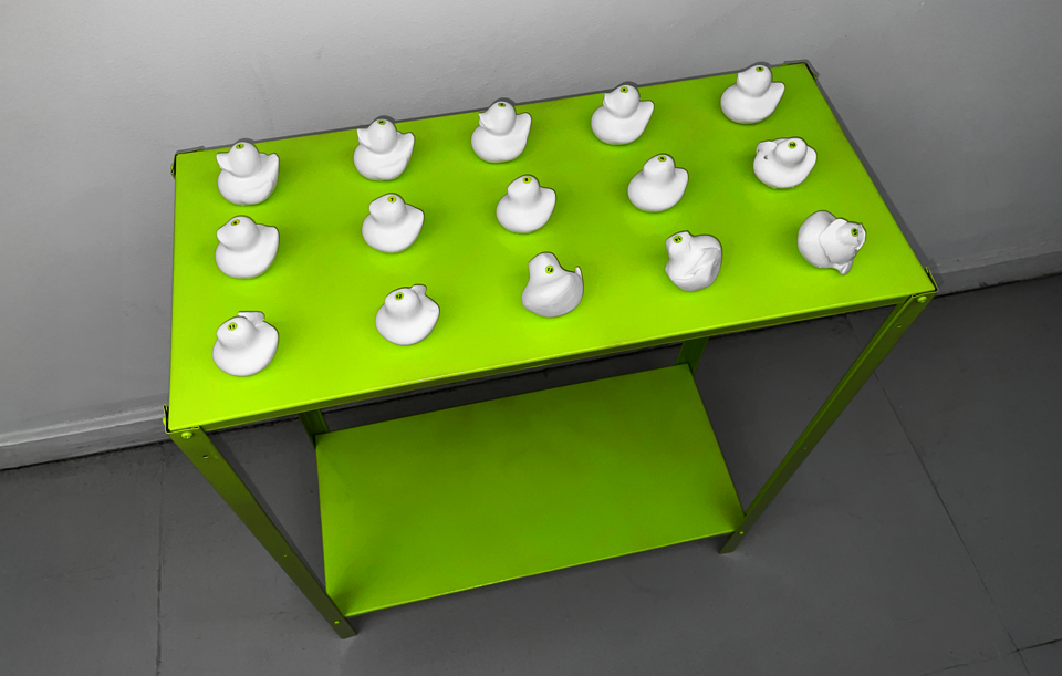 3D-printed white duck sculptures on a lime green shelf, each slightly distorted with numbered stickers indicating sequence.