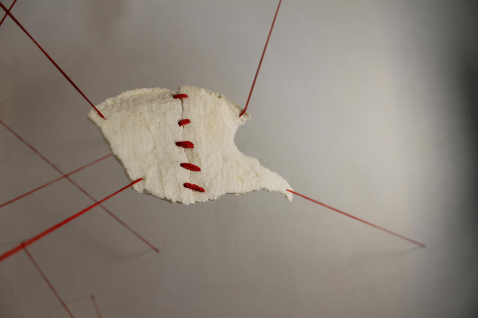 Fragmented pieces of Nablus soap stitched at the center with red thread, suspended with threads pulling from each corner.
