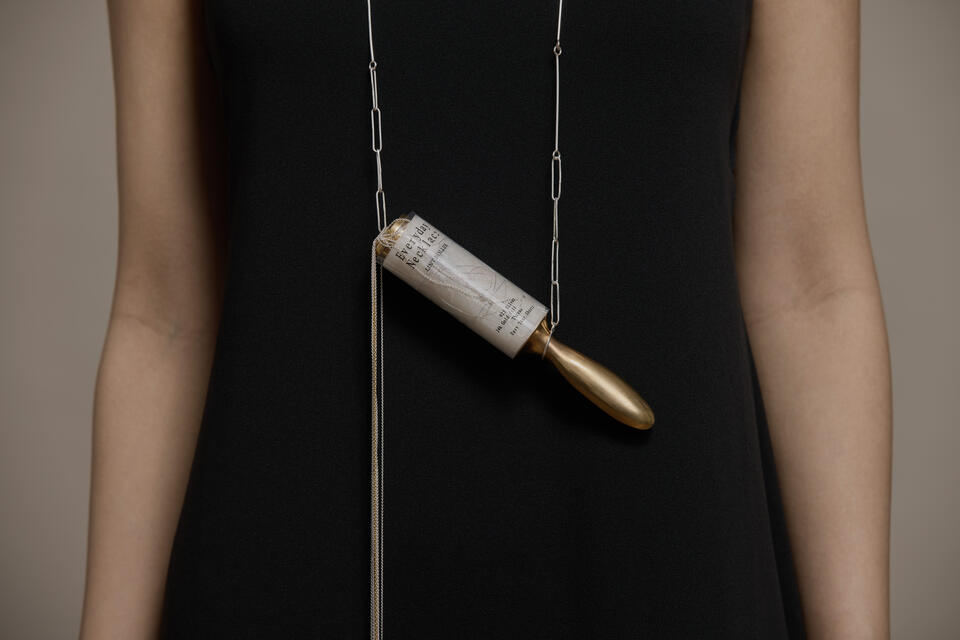 Necklace with metal lint roller pendant; segments tear off as individual pieces, titled and packaged “Everyday Necklace.”