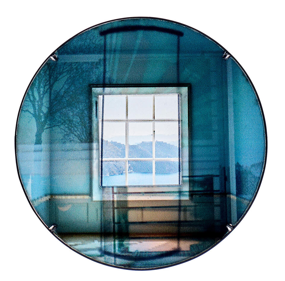 Blue circular brooch showing a square window view, with layered tree shadows and abstract light blending in a dreamlike room.