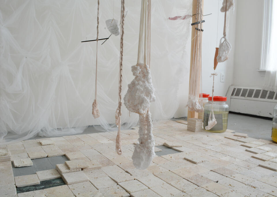 An installation of travertine tiles below threads that wrap around pieces of glass and coated in salt.