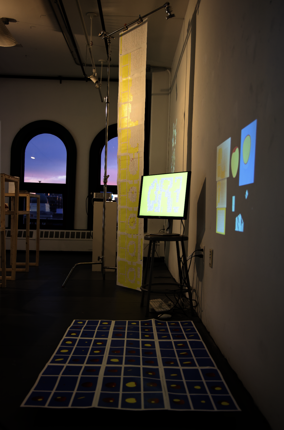 Art installation with hanging scroll, digital screen, projection, and blue grid of circular prints on the floor