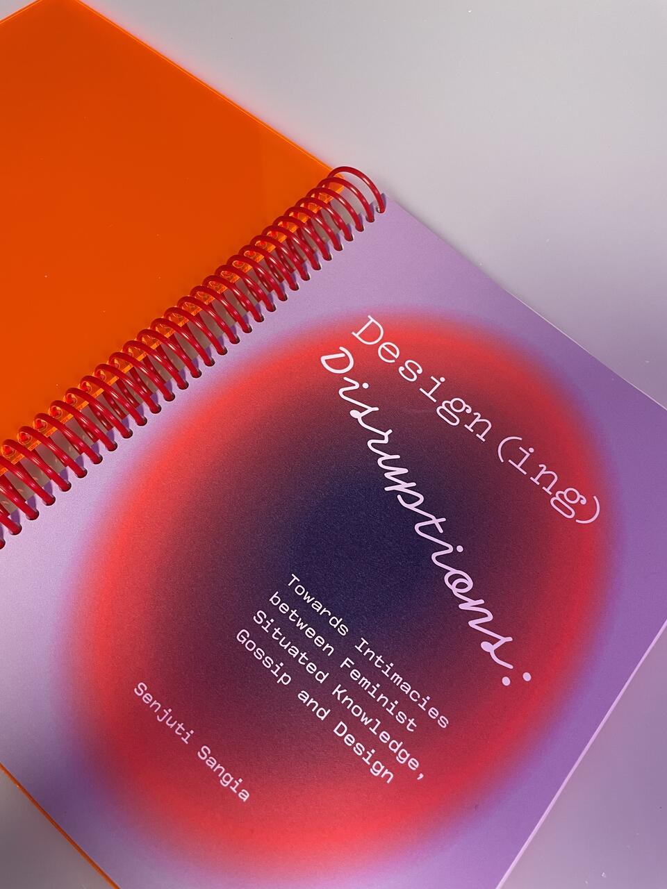 A lilac and orange cover of a spiral-bound book titled Design(ing) Disruptions by Senjuti Sangia. 