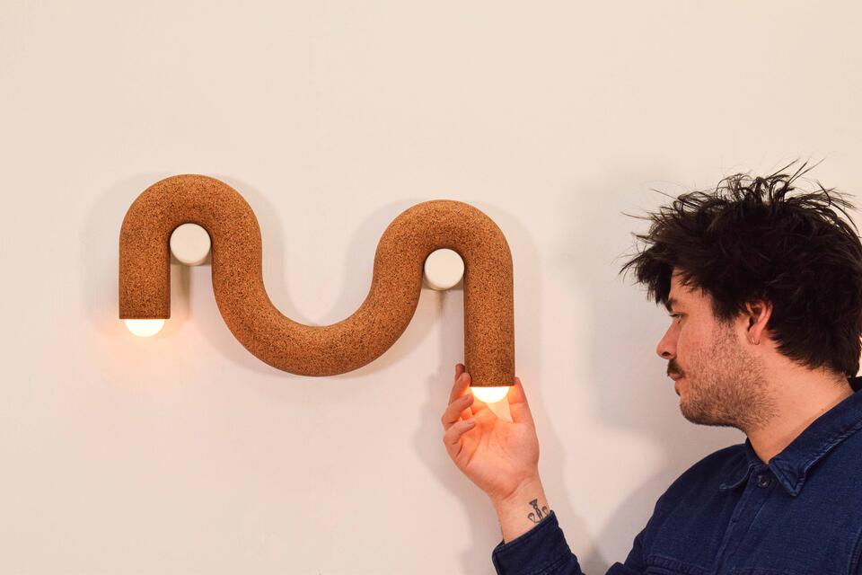 A brown cork cylinder droops over two white pegs like a noodle; bulbs protrude from both ends.