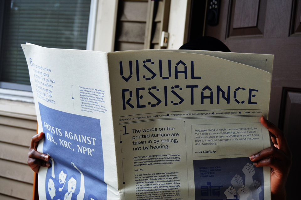 Person holding open 'Visual Resistance' newspaper, face hidden, hands gripping the spread.