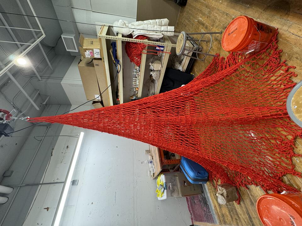 Red net hanged with ceramic objects dangled from a hoist. Hoist perform motion of let net spread on floor and pull it back up