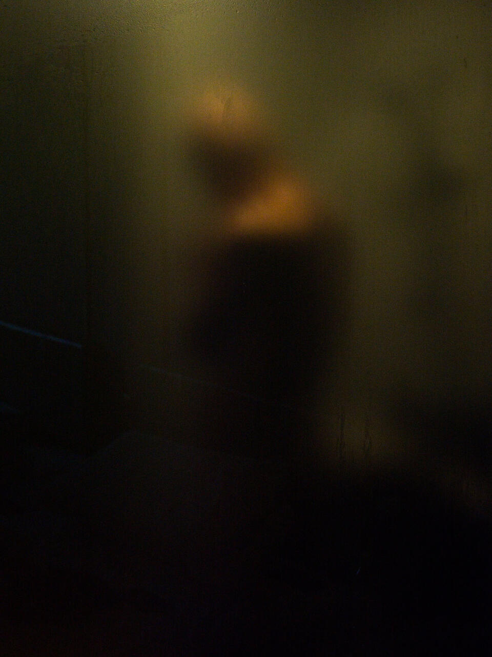A shadowy silhouette of a man bathing behind translucent hotel glass, soft light creating intimacy and emotional distance.