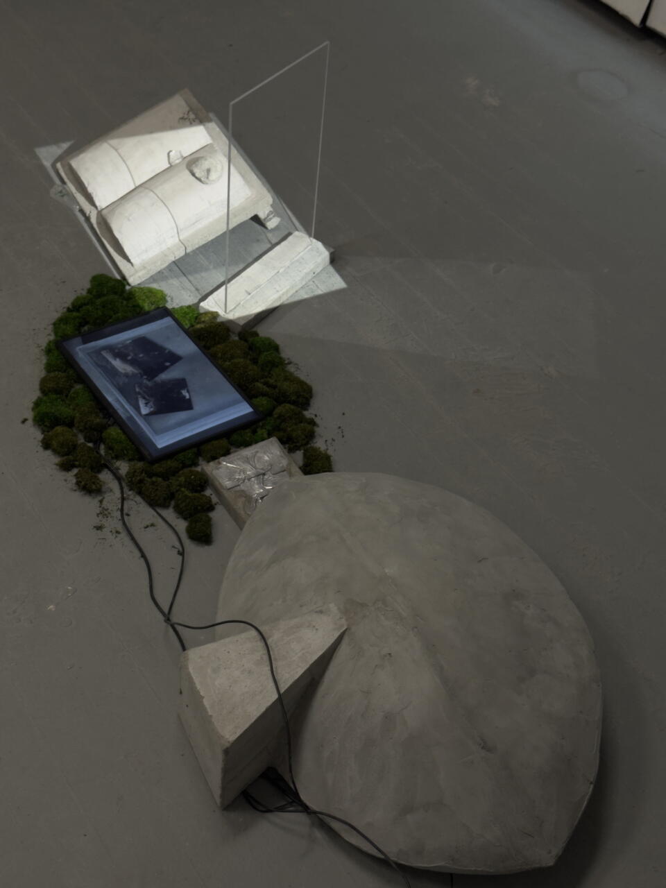Concrete dome, moss-framed screen with floating mirrors, and book-like slab lit by dripping water’s shadow through glass.